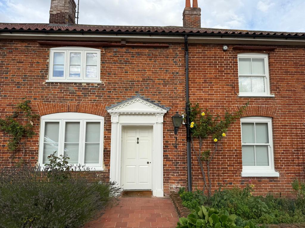 A red-brick Norfolk cottage with freshly repainted white sash windows and front door