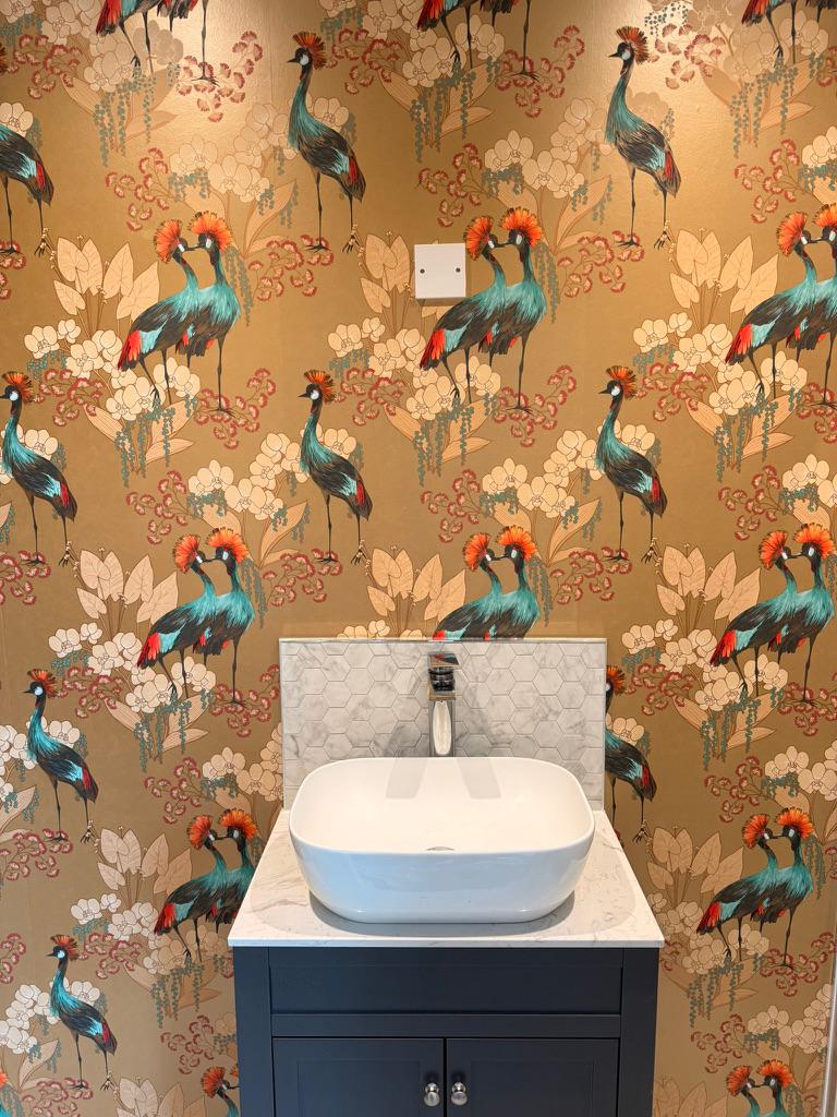 A cloakroom with gold crane-pattern wallpaper above a navy vanity