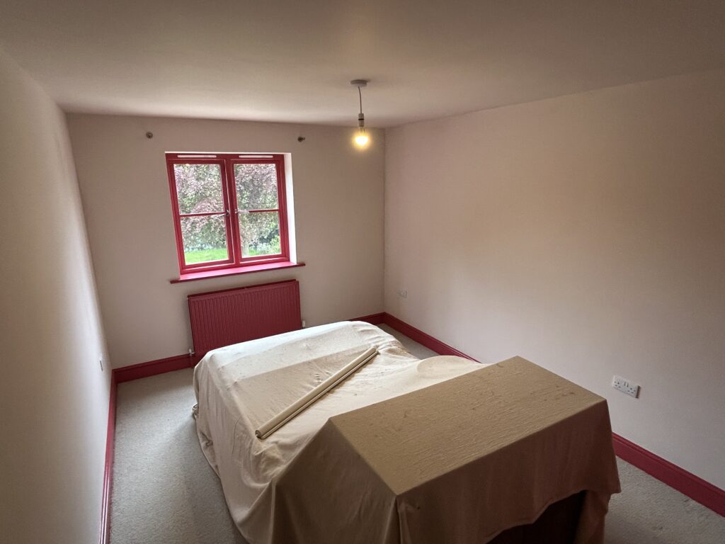 Small bedroom with red window frame and radiator